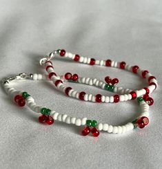 two white and red beaded bracelets with bells on the ends, sitting on a bed