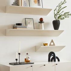 two white shelves with candles, vases and other items on them in a living room