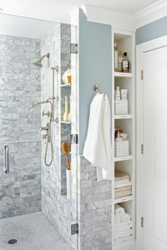 a walk in shower sitting next to a white door and shelves filled with toiletries