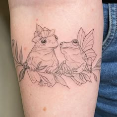 two frogs sitting next to each other on a branch with leaves and flowers around them