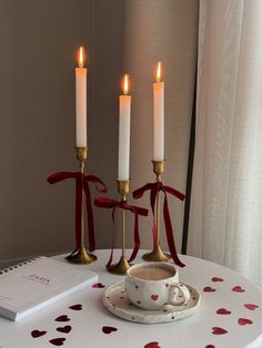 three candles are lit on a table with a cup and saucer