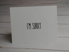 i'm sorry written on a white card with black ink, sitting on a wooden surface