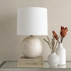 two vases with flowers sit on a shelf next to a lamp