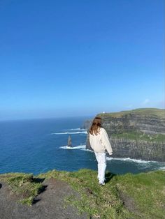 a woman standing on top of a cliff overlooking the ocean with cliffs in the background