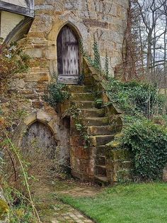 an old stone building with steps leading up to the front door and green grass growing around it