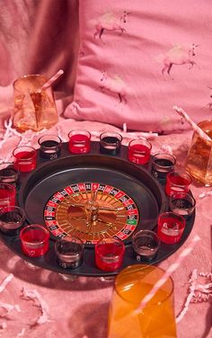 a casino roule surrounded by shot glasses and shots on a pink tablecloth with candles