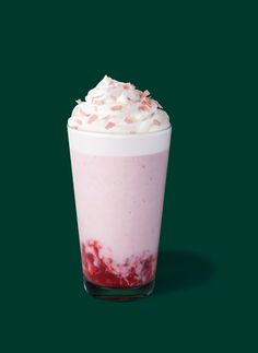 a drink with whipped cream on top is sitting next to a dark green background and has pink sprinkles in it