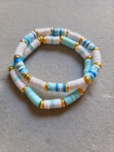 three bracelets with blue, white and gold beads on top of a gray surface