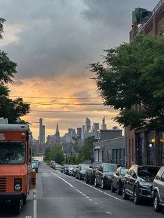 cars parked on the side of a street in front of a city skyline at sunset