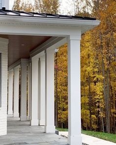 a white building with columns and a clock on the front porch next to trees that have yellow leaves