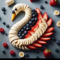 an animal made out of bananas, strawberries and blueberries on a gray surface