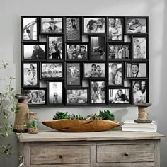 a wooden table topped with a bowl filled with flowers next to a wall covered in pictures