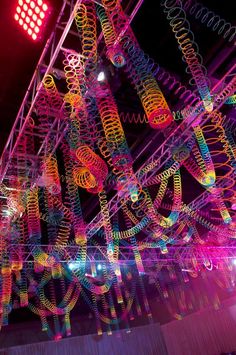 an art installation is lit up at night with colorful lights and spirals hanging from the ceiling