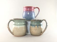 three mugs are stacked on top of each other in different colors and shapes,