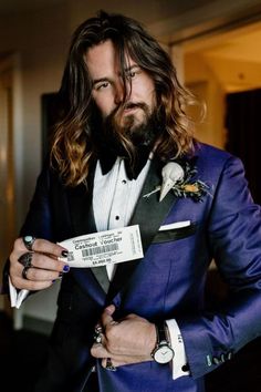 a man with long hair wearing a blue suit and bow tie holding a ticket in his hand