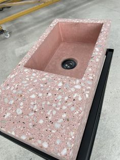 a pink sink sitting on top of a black stand in a room with concrete flooring