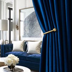 a living room with blue velvet curtains and white pillows on the couches in front of a large mirror