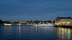 boats are docked in the water at night near some buildings and lights on the shore