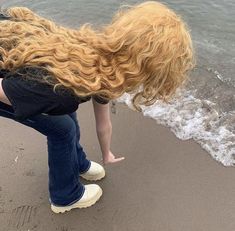 a woman bending over on the beach with her hair blowing in the wind and water behind her