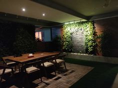 an outdoor dining area with wooden table and white chairs, surrounded by greenery on the wall