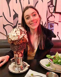 a woman sitting at a table in front of a bowl of ice cream and salad