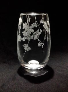 a clear glass with white flowers and leaves on the inside is sitting on a black surface