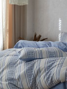 an unmade bed with blue and white comforter next to a window in a bedroom