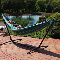 a woman laying in a hammock on a brick patio next to a pond