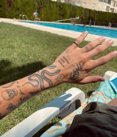 a man with tattoos on his arm sitting next to a swimming pool