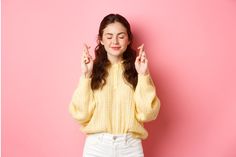 a woman standing in front of a pink wall holding her hands up to the side