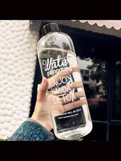 a person holding up a water bottle with the words water on it in front of a building