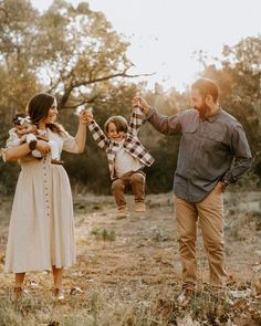 a man and woman holding two small children in their hands while they walk through the woods