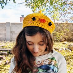 a girl wearing a yellow crocheted hat with black eyes and an orange bird on it