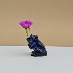 a frog figurine sitting next to a purple flower on top of a table