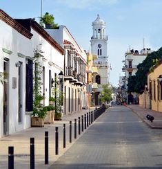 an empty street lined with white buildings and tall clock tower in the backgroud