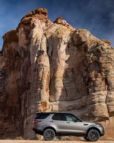 a silver suv parked in front of a large rock formation on the side of a road