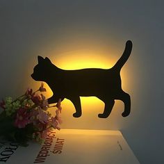 a cat lamp sitting on top of a book next to flowers and a vase with pink flowers