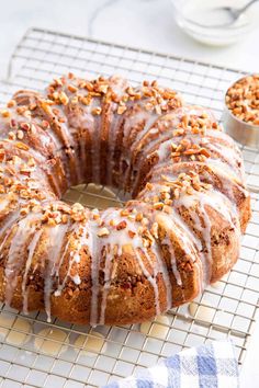 A golden bundt Sock It To Me Cake topped with a sweet glaze and chopped pecans, resting on a cooling rack with a small bowl of pecans in the background.