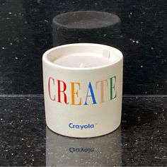 a coffee cup with the word create on it sitting on a black countertop next to a white candle holder