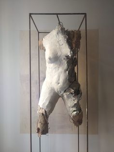 a white sculpture in a metal frame on top of a wooden floor next to a wall