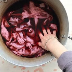 a woman's hand is reaching into a pot full of red dye and cloth