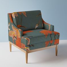 an upholstered chair with colorful birds on it's back and arms, against a blue background