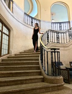 a woman in a black dress is walking down some stairs