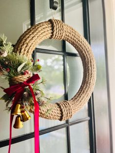 a wreath hanging on the front door with a red ribbon and bells attached to it