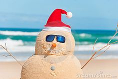 a sand snowman wearing sunglasses and a santa hat