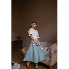 a woman in a white shirt and blue skirt standing next to a couch with pillows