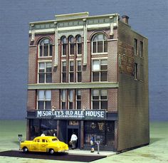 a yellow car is parked in front of a tall brick building with people walking by