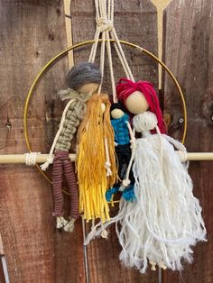 three dolls are hanging from a hoop on a wooden fence with ropes and yarn around them