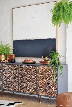 a black and gold sideboard with potted plants on it in front of a white brick wall