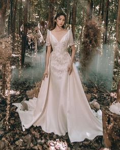 a woman standing in the woods wearing a wedding dress